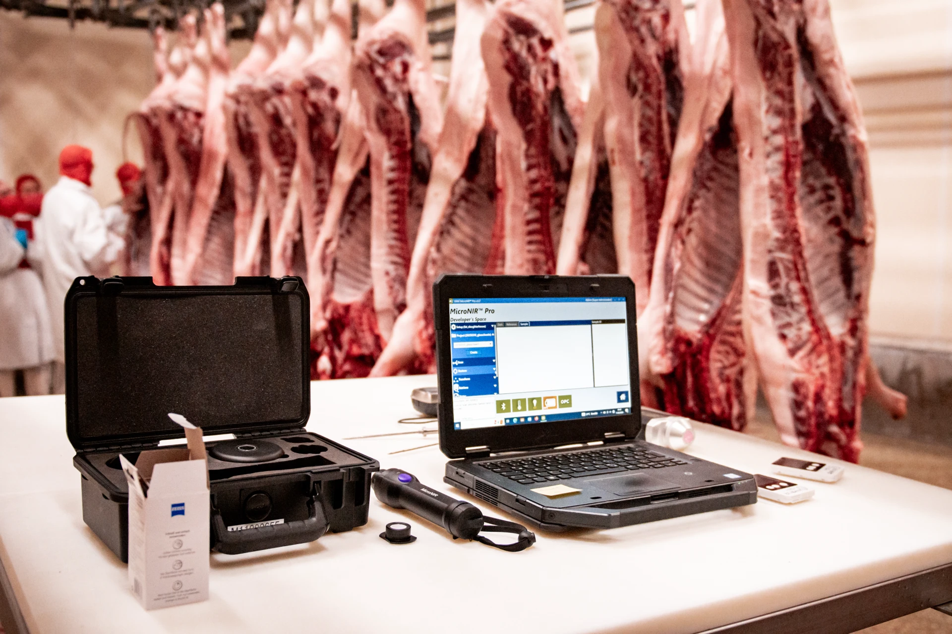 Messtechnik für Fleischkontrolle im Schlachthof, Schweinehälften im Hintergrund, Qualitätsprüfung, Laborgerät.